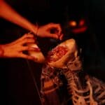 The 5 Best Halloween Candy Packs for Tippah County Trick-or-Treaters A Halloween candy bowl shaped like a skull filled with wrapped candies, with hands adding more treats — spooky trick-or-treat setup