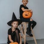 The 5 Best Halloween Costumes for Tippah County Kids Two kids with carved jack-o'-lanterns, one wearing a witch hat