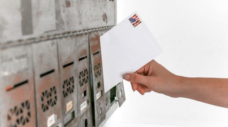 Hand dropping a stamped envelope into a mailbox, illustrating absentee voting by mail