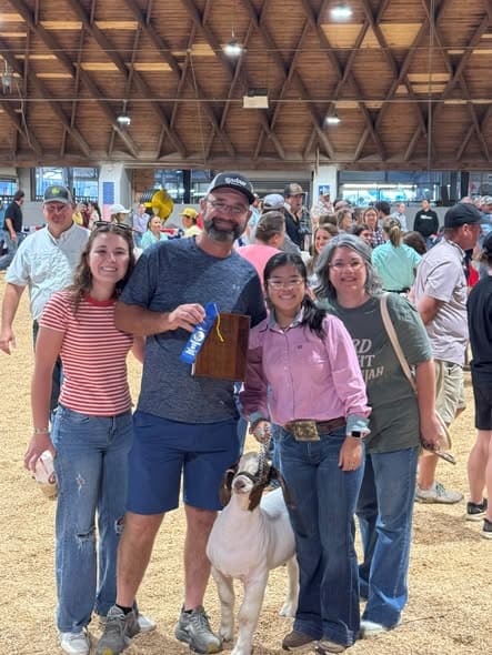 Tippah County 4-H exhibitor with her market goat, a ribbon and family at the Mississippi State Fair goat show